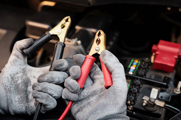 Close-up hand auto mechanic using connect jumper cable on terminal dead battery for jump-start or check car battery fail problem to change repairing and fix car and maintenance servicing.