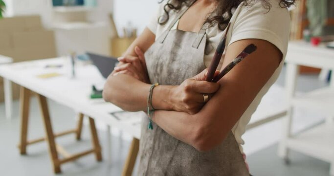 Artist in a studio, arms crossed holding a paintbrush