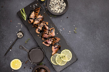 sliced pieces of Organic grilled Tuna Steak on black stone serving board and teriyaki soy sauce