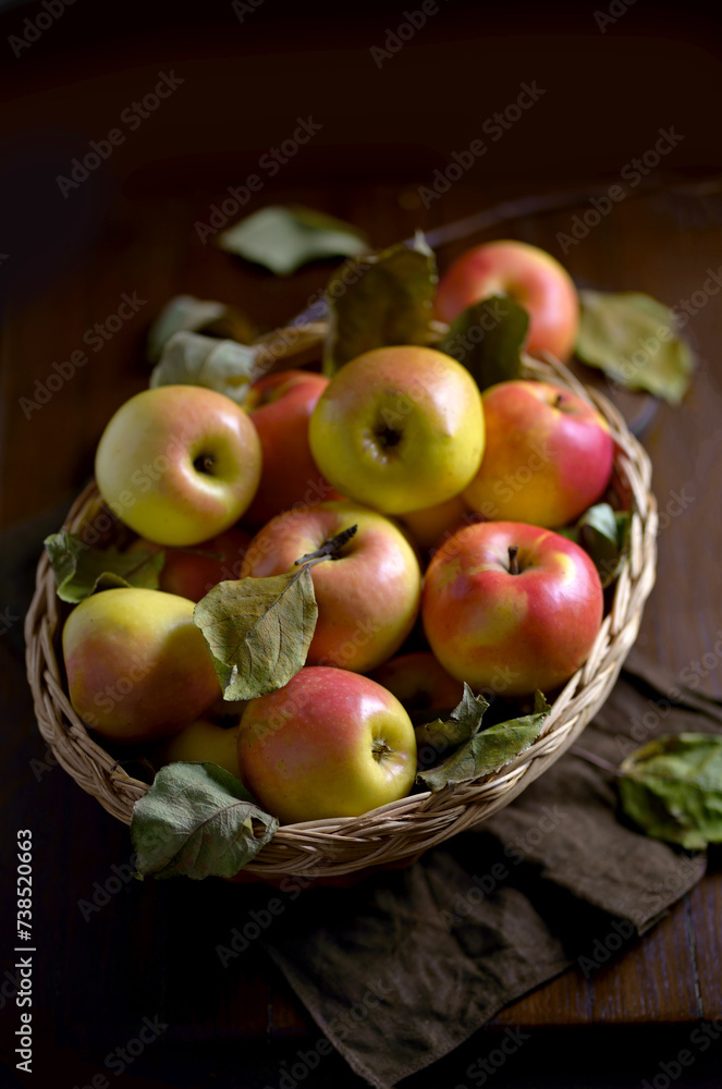 Poster Apples in a basket on a wooden table. Fresh red apples with green leaves on a black background. Fruits. View from above.