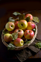 Apples in a basket on a wooden table. Fresh red apples with green leaves on a black background. Fruits. View from above.