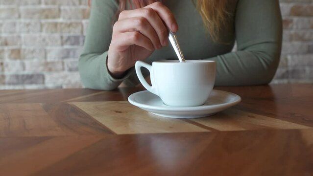 Close-up of a woman's hands stirring a white coffee cup