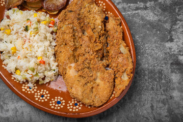 Breaded fried fish and rice in a clay dish on a wooden table.