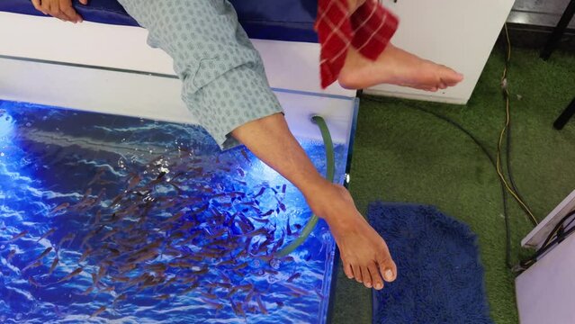 women receiving a fish pedicure therapy with small fish nibbling at their feet in a blue water in fish spa and wiping legs