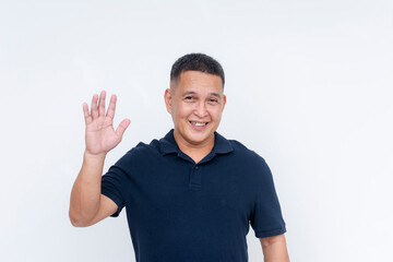 Cheerful middle-aged Asian man in a casual polo shirt waving hi with a warm smile, isolated on a...