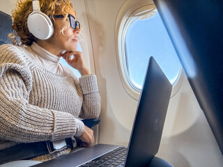 Woman passenger sitting inside the airplane flight enjoying the travel listening music or watching...