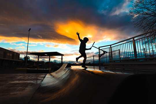 Silhouette of boy riding scooter on skate park ramp at sunset in Mansfield, Victoria