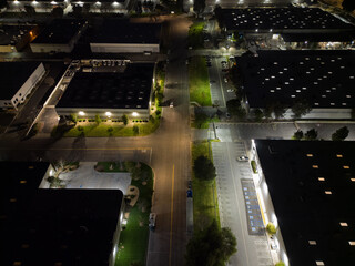 Several warehouse buildings along the street of an industrial park are shown from an aerial view late at night.