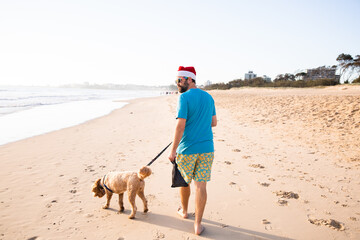 man wearing a santa hat walking a dog on the beach