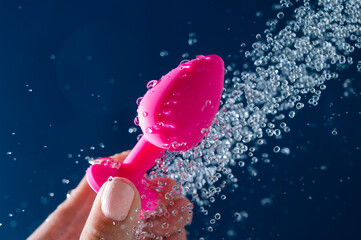 Woman washing pink anal plug under shower on blue background. 