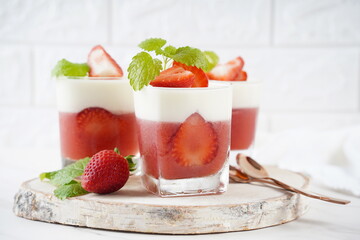 Vanilla panna cotta with strawberry layer in a small portioned vase and fruit pieces in...
