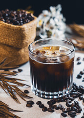 Ice coffee black in a glass and coffee beans. Cold summer drink on wooden table with copy space....