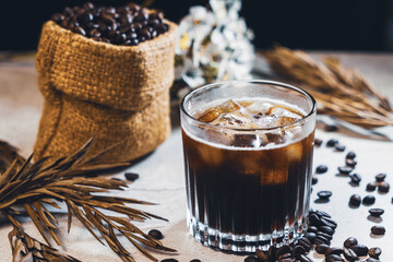 Ice coffee black in a glass and coffee beans. Cold summer drink on wooden table with copy space....