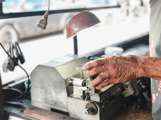Locksmith Crafting Keys on Professional Equipment. A locksmith's skilled hands working on key-cutting equipment under a task light in a workshop.
