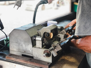 Locksmith Crafting Keys on Professional Equipment. A locksmith's skilled hands working on key-cutting equipment under a task light in a workshop.
