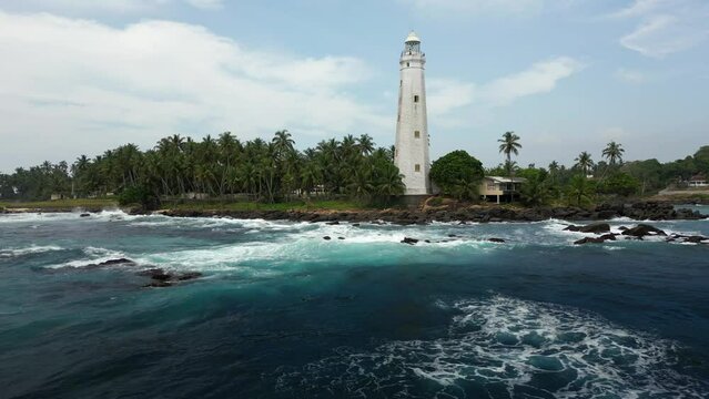 White colonial Dondra Head lighthouse surrounded by the stormy ocean, waves and palms on the jungle coast of Sri Lanka