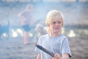 Boy surrounded by smoke holding burning stick with brother and pet lamb in background