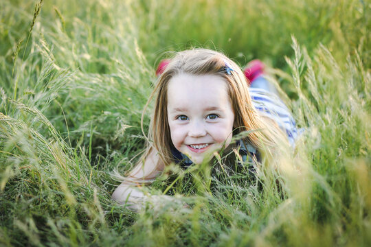 Caucasian girl with long hair lying in long grass at the park with a big smile
