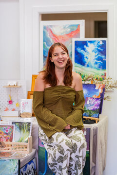 Young artist in her early twenties sitting at art market stall pop up shop