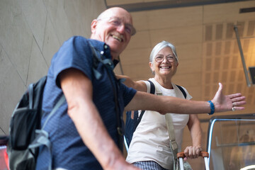Smiling senior couple in airport departure area on escalators going towards boarding. Travel and...