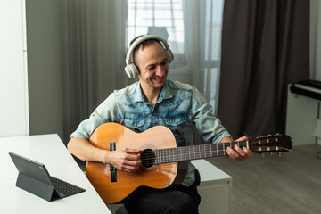 Obraz premium 40 years old man playing the guitar at home and using a laptop