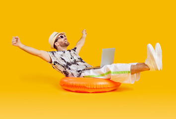 Happy businessman entrepreneur worker finishes remote work on computer on summer holiday trip vacation. Relaxed tourist man rests on comfortable orange ring with laptop PC on yellow studio background