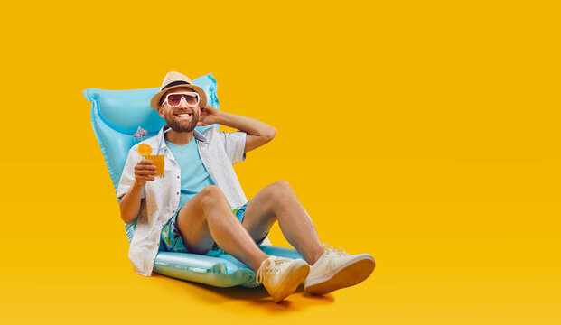 In the spirit of summer holidays, a man lounges on an inflatable mattress, in summer attire. With a cocktail in hand, he exudes relaxation on a orange backdrop, capturing carefree vacation moment.
