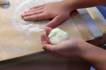 Preparation of homemade fruit dumplings with plums. Czech specialty of sweet good food. Dough on kitchen wooden table with hands.