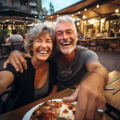 Foto auf Glas Happy senior old couple have fun eating a pizza together outdoor in traditional italian pizzeria restaurant sitting and talking and laughing. People enjoying food and elderly lifestyle. Tourism © simona