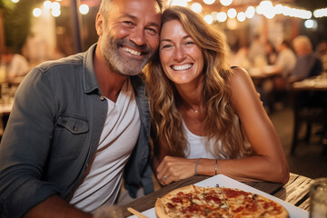 Happy adult cute couple have fun eating a pizza together outdoor in traditional italian pizzeria restaurant sitting and talking and laughing. People enjoying food and travel lifestyle. Tourism