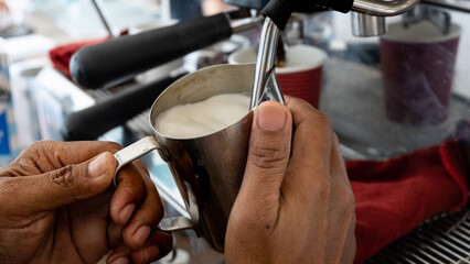 Close up of barista steaming hot frothy milk from stainless steel coffee machine in local coffee...