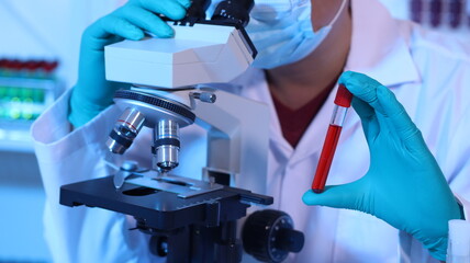 Scientists are doing research in a science lab. A medical chemist in a white coat, gloves and goggles looks at a glass tube. Compare two different liquid samples. and discuss future experiments.