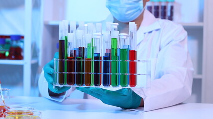 Scientists are doing research in a science lab. A medical chemist in a white coat, gloves and goggles looks at a glass tube. Compare two different liquid samples. and discuss future experiments.