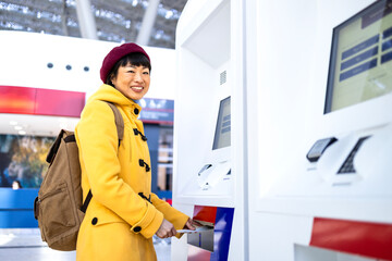 Female passenger with backpack printing boarding pass at self-service kiosk at the airport.