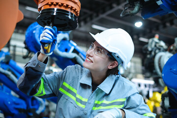 Caucasian female engineer using pliers to adjust screws of industrial robot arm in factory.