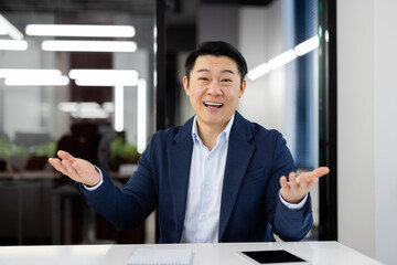 Asian businessman in a suit gesticulates while explaining a concept or giving a presentation in a...