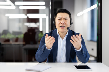 An Asian businessman in a modern office feels frustration during a call. Customer service...
