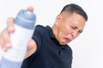 Man with a disgusted expression using air freshener spray to combat a foul smell, isolated on white...