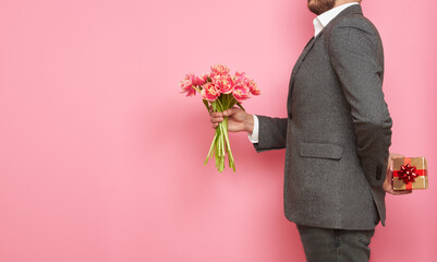 Romantic man in suit, with gift box and bouquet of tulips on isolated pink background, Valentine's Day, March 8 - obrazy, fototapety, plakaty