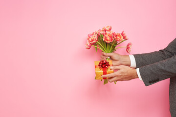 Romantic man presents a gift box and bouquet of tulips on isolated pink background, Valentine's...
