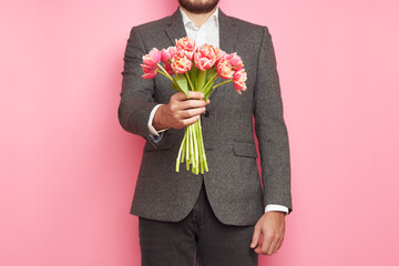 Romantic man in suit, with bouquet of tulips on isolated pink background, Valentine's Day, March 8