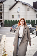 a beautiful woman with red hair in a gray coat walks through the city