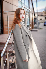 a beautiful woman with red hair in a gray coat walks through the city