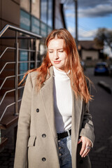 a beautiful woman with red hair in a gray coat walks through the city