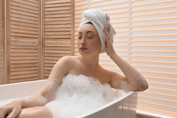Beautiful woman taking bath with foam in tub indoors