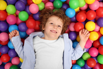 Fototapeta na wymiar Happy little boy lying on many colorful balls, top view