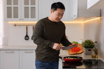 Cooking process. Man adding cut bell pepper into frying pan in kitchen, space for text