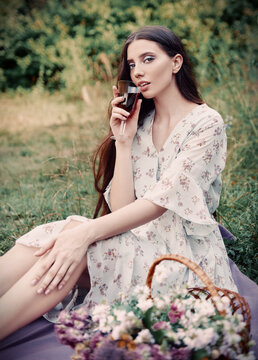 Picnic scene: adorable sensual girl sitting on plaid in park and drinking juice (wine). Outdoor portrait of beautiful young woman in dress. Effect of old faded film. Vintage look