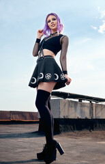 Portrait of cheerful smiling gothic girl on roof. Pastel goth with violet (purple) hair in black...