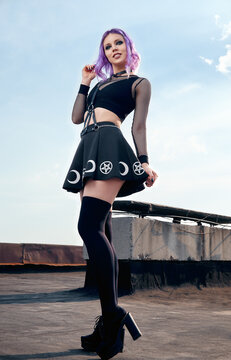 Portrait of cheerful smiling gothic girl on roof. Pastel goth with violet (purple) hair in black clothes